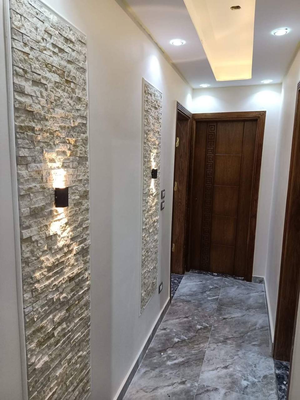 Hallway with stacked stone accent walls and tile flooring